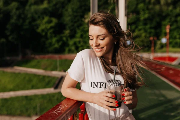 Bermimpi wanita bahagia mengenakan t-shirt putih minum kopi pagi dan berjalan di jalan cerah dengan senyum bahagia — Stok Foto