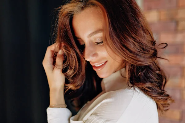 Tutup potret studio wanita Eropa yang menarik dengan rambut keriting yang berpose di atas dinding hitam dan tersenyum — Stok Foto