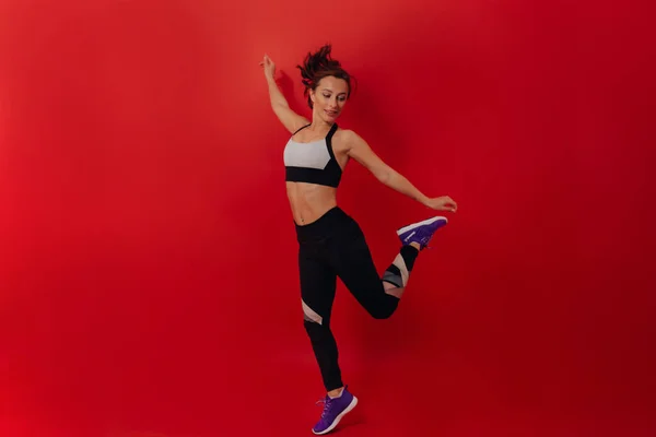 Спорт и здоровая концепция. Спортивная привлекательная женщина в спортивной форме прыгает через красный фон — стоковое фото