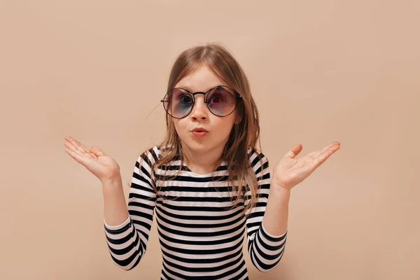 Engraçado bonito menina 6 anos de idade posando na câmera sobre fundo bege com emoções verdadeiras surpresas — Fotografia de Stock