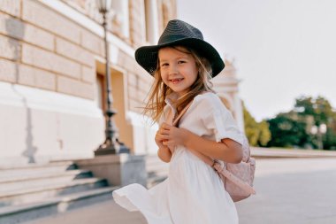 Şık çocuk 6 yaşında beyaz yazlık elbise ve şapka giyen yaz yürüyüş zevk ve dışarıda eğleniyor 
