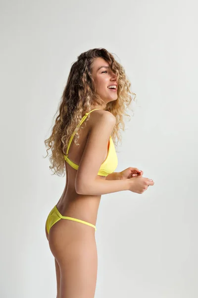 고립 된 배경에 포즈를 취하는 노란색 수영복을 입고 물결 모양의 긴 머리를 가진 행복한 웃는 금발의 여자 — 스톡 사진