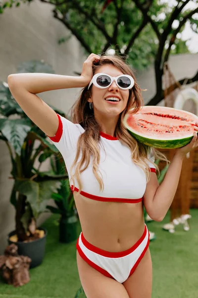 Draußen Foto von attraktiven jungen Frau trägt Badeanzug und weiße Modebrille und hält Wassermelone — Stockfoto