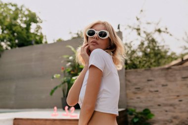 Egzotik bitkiler üzerinde poz beyaz üst ve güneş gözlüğü giyen kısa saç modeli ile etkili şık sarışın kadın 