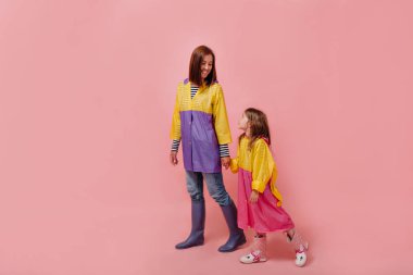 Kadın i ile yağmurluk sevimli çocuk kız bebek. Anne, küçük çocuk kızı pastel pembe duvar arka plan izole