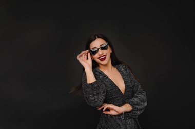 Parlak elbiseli ve gözlüklü tutkulu beyaz kız karanlık arka planda doğum günü fotoğraflarının keyfini çıkarıyor..