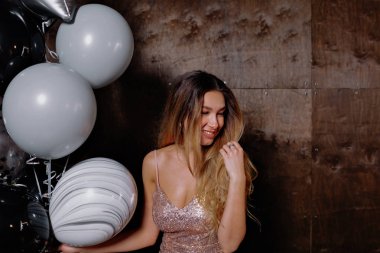 Sarışın, çekici, balonlu ve konfetili parlak elbiseli bir kızın portresinin içinde izole edilmiş karanlık arka planda poz verdirilmiş.