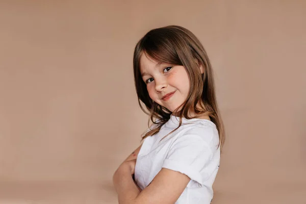 Tutup potret studio dalam ruangan gadis kecil cantik dengan rambut panjang mengenakan t-shirt putih berpose di atas latar belakang terisolasi dan tersenyum di depan kamera — Stok Foto