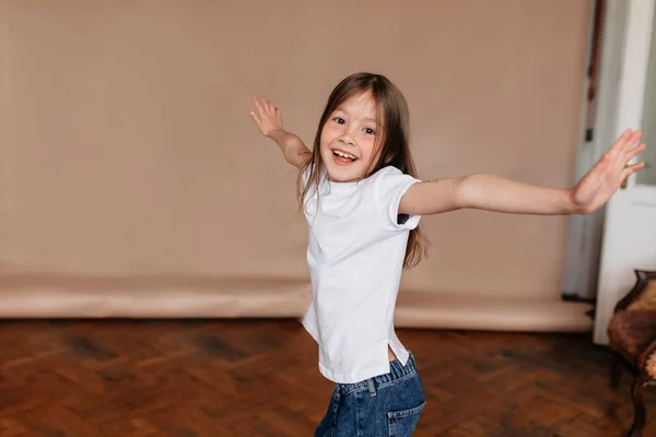 Happy keluar gadis kecil mengenakan t-shirt putih dan jeans menari dan bersenang-senang di atas latar belakang terisolasi selama pemotretan — Stok Foto