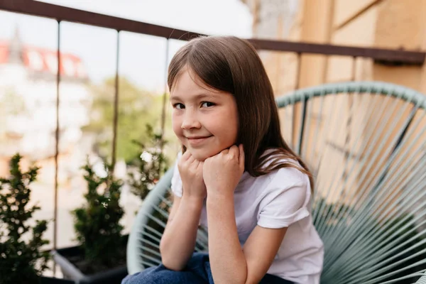 Di luar close up potret indah gadis kecil yang lucu duduk di balkon dan berpose di kamera di latar belakang musim panas — Stok Foto