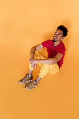 Parlak elbiseli sevimli gülümseyen adamın izole edilmiş sarı arka planda oturduğu bir stüdyo resmi.