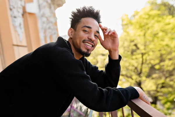 Retrato al aire libre de un hombre afro americano feliz sonriente con un jersey negro posando en la cámara en la terraza al aire libre —  Fotos de Stock