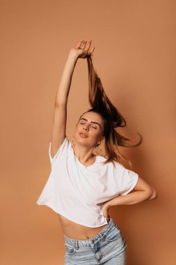 Gülümseyen, kapalı gözlerle poz veren ve saçlarıyla izole edilmiş bej arka planda oynayan muhteşem güzel bir kadın manken. 