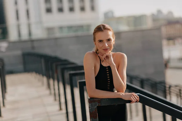 Sonriente mujer bastante europea posando en la cámara con sonrisa mientras entrena al aire libre en un día soleado —  Fotos de Stock