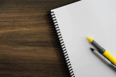 Ahşap arka plan üzerinde vurgulayıcı ve kalemli spiral not defteri kağıdı