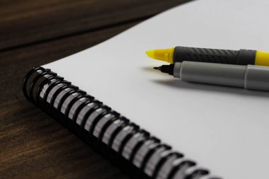 Ahşap arka plan üzerinde vurgulayıcı ve kalemli spiral not defteri kağıdı