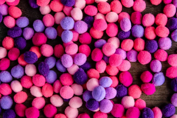 Round pink and purple fluffy balls pompoms on wooden background
