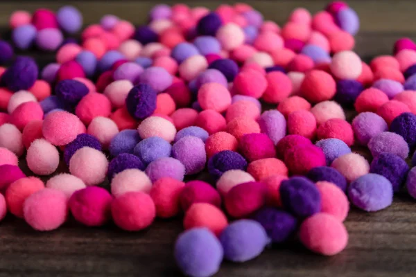 Round pink and purple fluffy balls pompoms on wooden background
