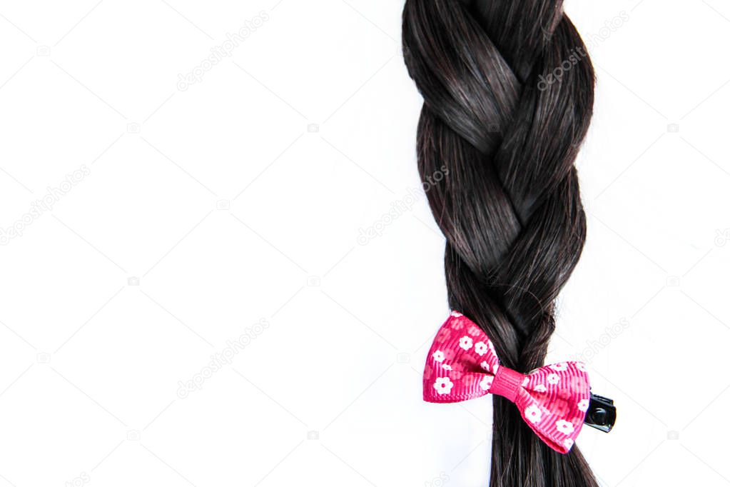 Black dark braided hair with pink bow isolated on white background. Brunette natural braided hair extension with pink hair pin on white background