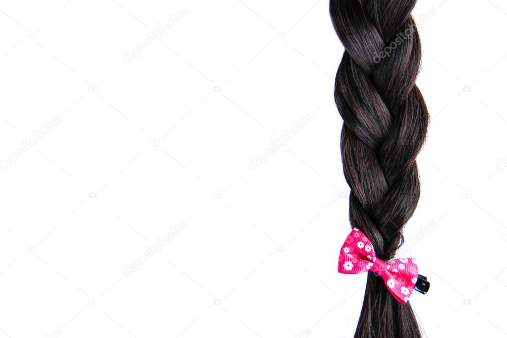 Black dark braided hair with pink bow isolated on white background. Brunette natural braided hair extension with pink hair pin on white background