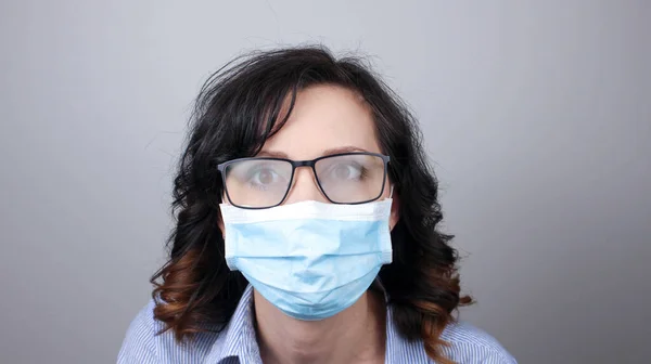 Koronavirüs ve sisli gözlüklere karşı koruma maskesi takan bir kadın. Aynaya bakan maskeli bir kadın. Tıbbi maske, yakın çekim, odaklanmayı seç, covid19 'u önle.
