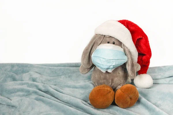 A sick sad plush toy in a mask and Christmas hat. Flu colds disease virus bacterium. Plush donkey toy wear protection mask and Santa hat, Protect Against Coronavirus concept