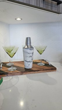 Stylish cocktail shaker with a marble finish sits on a wooden tray, flanked by two martini glasses filled with green beverage, enhancing bar aesthetics