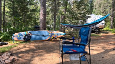 Ottawa ON, Canada - July 26, 2025: Camping setup includes a blue paddleboard, a comfortable chair, and a hammock surrounded by tall trees and nature