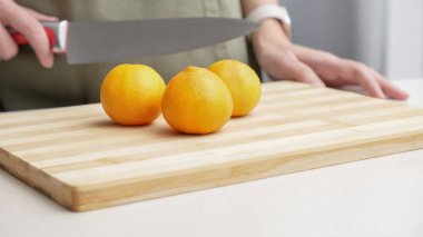 Masadaki kesme tahtasının üzerinde portakal renginde mandalina kesen eller, yemek yapmak için bir sürü sulu taze meyve..