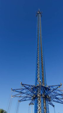 Amusement park ride structure rises high against a vibrant blue sky, highlighting intricate engineering and inviting excitement for thrill-seekers