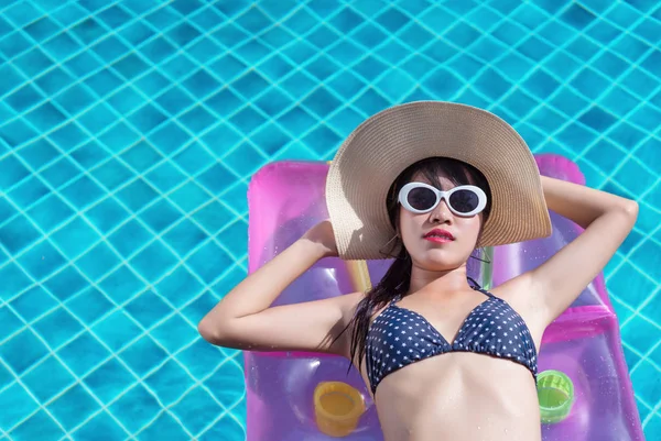 Woman asian bikini swimming pool on rubber float with sun hat relaxing vacation enjoying on tropical summer season, copy space the left.