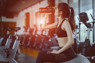Genç Asyalı kadın protein sallamak için yoga topu üzerinde oturan fitness spor salonu sağlıklı yaşam vücut geliştirme kas egzersiz egzersiz sonrası Şişeden içme