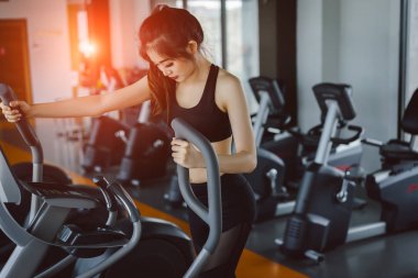 Asyalı kadın egzersiz eliptik kardiyo egzersiz fitness salonunda sabah ince ve sert sağlıklı yaşam için aerobik makine ile kilo kaybı alarak çalışan.