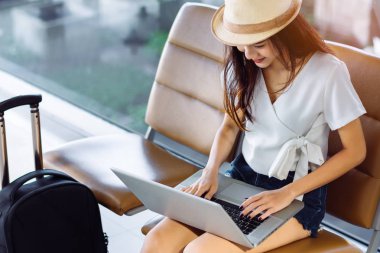Havaalanı Bagaj bavul ve seyahat bekleyen uçuş taşıma rahatlatıcı tatil yaz aylarında için sırt çantası ile oturan terminal dizüstü bilgisayar kullanan Asyalı kadın genç
