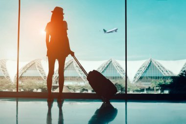 Silhouette woman travel with luggage looking without window at airport terminal international or girl teenager traveling in vacation summer relaxation holding suitcase and backpack clipart
