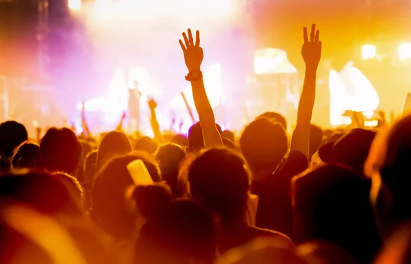 Crowd of concert stage lights and people fan audience silhouette raising hands or glow stick holding in the music festival rear view with spotlight glowing effect