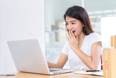Genç Asyalı kadın iş tepki yaz Satılık moda online sürpriz ahşap masa evde çalışma üzerinde oturan dizüstü bilgisayar office Not ile bakarak şok.