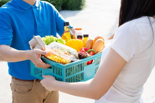 Food Deliver Asian man in blue uniform give fruit and vegetable to receiver customer front house, fast express grocery service when crisis coronavirus, covid19 new normal lifestyle concept.