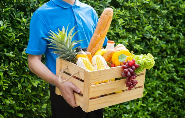 Food Deliver Asian man in blue uniform give fruit and vegetable to receiver customer front house, fast express grocery service when crisis coronavirus, covid19 new normal lifestyle concept.