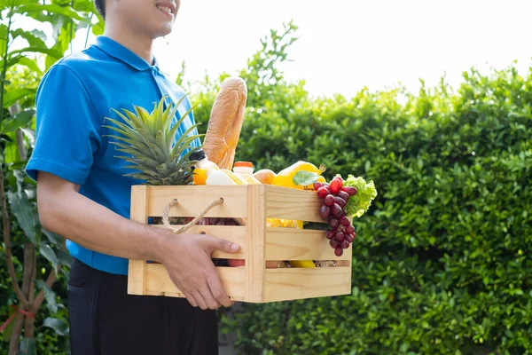 Food Deliver Asian man in blue uniform give fruit and vegetable to receiver customer front house, fast express grocery service when crisis coronavirus, covid19 new normal lifestyle concept.