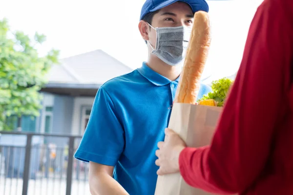 Food Delivery man wearing mask give fruit and vegetable shopping supermarket to receiver woman customer front house, express grocery service when crisis coronavirus, covid19 new normal lifestyle.