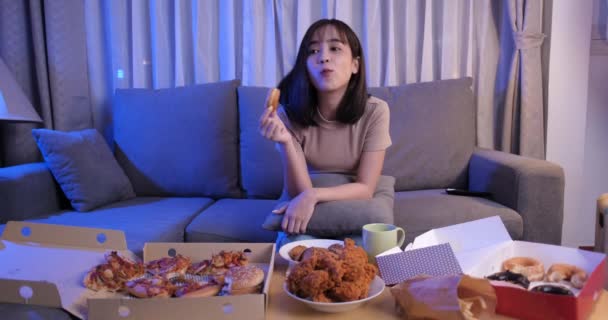 年轻的亚洲女人带着满满的垃圾食品 坐在沙发上 在客厅里看电视 在家里的快餐店里 她已经试着睡觉了 — 图库视频影像