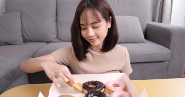 Ung Asiatisk Kvinna Takeaway Äta Munk Skräp Mat Soffan Vardagsrummet — Stockvideo