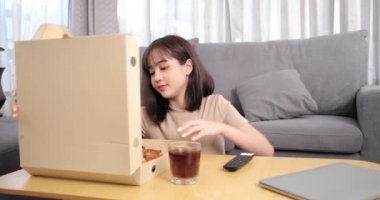 Genç Asyalı bir kadın abur cubur yiyip kola içiyor ve uzaktan kumandalı bir kadın kullanıyor. Mutluluğun tadını çıkarıyor ve evde televizyon seyrediyor. Fast food servis konsepti..