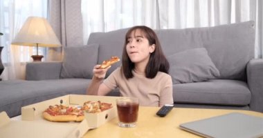 Genç Asyalı kadın kolayla pizza yiyen abur cubur alıyor. Kadın evde yemek yiyip televizyon izlemekten zevk alıyor. Fast food servis konsepti.