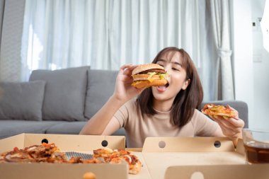 Asyalı kadın hazır yemek ve pizza yerken eve yakın çekim, Fast Food teslimat servisi güvenli ve Coronavirus 'un sosyal uzaklık konseptiyle yayılmasını engeller..