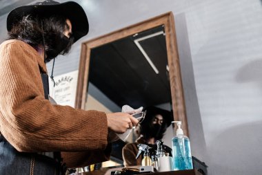Erkek berber temizlik ekipmanı saç kesiminden önce alkol spreyi ile saç kesme makinesi. Coronavirus kilitleme ameliyatından sonra yüz maskesi takıyor. Yeni erkek saç modelleme normal yaşam tarzı..
