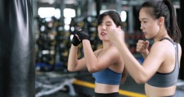 Sportif, genç Asyalı kadınlar boksör çalıştırıyor, koçla bileklerine kayış takıyorlar boks antrenmanı yapıyorlar spor antrenmanları yapıyorlar spor salonunda partnerleriyle spor yapıyorlar sağlıklı bir yaşam tarzı ve nefsi müdafaa kavramları var..