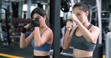 Sportif, genç Asyalı kadınlar boksör çalıştırıyor, koçla bileklerine kayış takıyorlar boks antrenmanı yapıyorlar spor antrenmanları yapıyorlar spor salonunda partnerleriyle spor yapıyorlar sağlıklı bir yaşam tarzı ve nefsi müdafaa kavramları var..