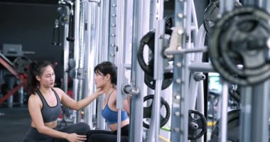 Sportif Asyalı kadınlar spor salonunda spor yaparken halterleri demirci makinesinde, kişisel antrenörleri sağlıklı vücut geliştirme eğitimi alırken sporcu kasları hayat tarzını geliştirir..